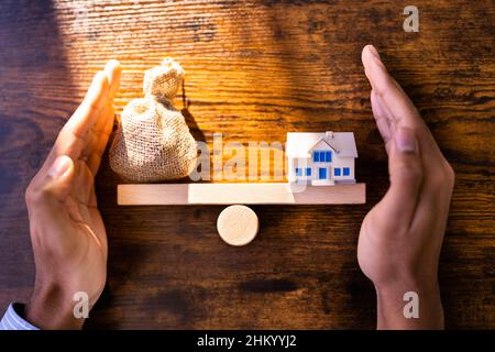 Primo piano della casa del modello e del bilanciamento dei soldi sulla bilancia di pesatura di legno Foto Stock