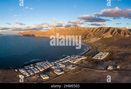 Caleta de Famara villaggio e Risco de Famara montagne sullo sfondo, Spagna Foto Stock