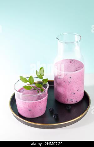 Bicchiere e bottiglia di frullato di mirtilli con foglie fresche su piastra rotonda su sfondo turchese. La bevanda sana è antivirale, utile per l'immunità. Tu Foto Stock