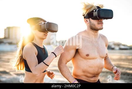 Coppia fitness in spiaggia con visore vr goggle - concetto di vita sportivo e tecnologico con persone moderne che fanno jogging e allenano sul trekking si Foto Stock