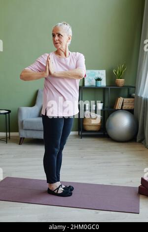 Donna anziana attiva moderna in leggins e t-shirt fare esercizio di yoga con le mani messe insieme di fronte a se stessa Foto Stock