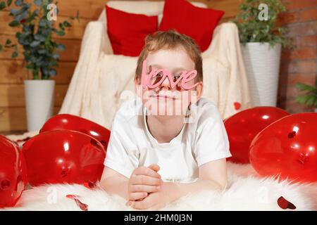 San Valentino bambini o bambini. Carino ragazzo gioioso con palloncini rossi a forma di cuore e testo amore a forma di occhiali, su San Valentino' Foto Stock