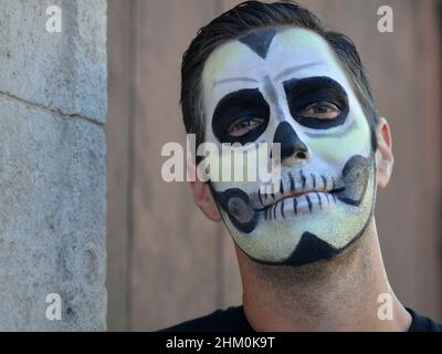 Il giovane uomo caucasico con la tradizionale pittura del volto bianco del giorno dei morti (Día de los Muertos) guarda verso il basso lo spettatore. Foto Stock