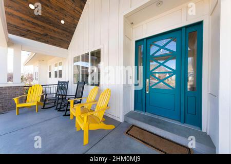 Elegante porta d'ingresso verde blu di una casa con due luci di posizione e campanello. Esterno di una casa con tavola bianca e falda e un portico con braccio Foto Stock