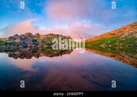 Cima e faccia occidentale del Cimon della pala, una delle cime principali del gruppo pala, ricoperta di nuvole, che si riflette in un lago al tramonto. Foto Stock