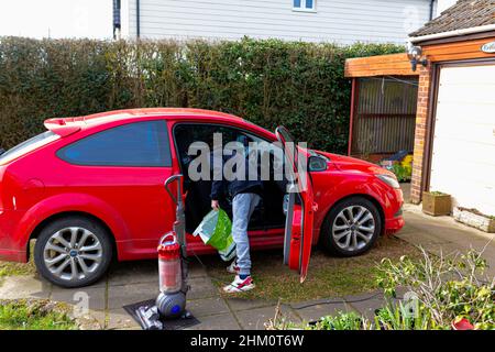 Woodbridge, Suffolk, UK Febbraio 24 2021: Un giovane uomo adulto che pulisce la sua auto. Pulizia dei rifiuti e aspirazione dello sporco e della polvere Foto Stock