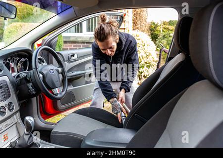 Woodbridge, Suffolk, UK Febbraio 24 2021: Un giovane uomo adulto che pulisce la sua auto. Pulizia dei rifiuti e aspirazione dello sporco e della polvere Foto Stock