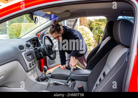 Woodbridge, Suffolk, UK Febbraio 24 2021: Un giovane uomo adulto che pulisce la sua auto. Pulizia dei rifiuti e aspirazione dello sporco e della polvere Foto Stock