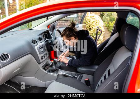 Woodbridge, Suffolk, UK Febbraio 24 2021: Un giovane uomo adulto che pulisce la sua auto. Pulizia dei rifiuti e aspirazione dello sporco e della polvere Foto Stock