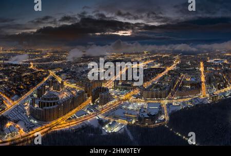 Paesaggio urbano invernale aereo di San Pietroburgo - Russia al crepuscolo, drone vola su enormi terreni abitati e parco pubblico, gru edili, notte Foto Stock