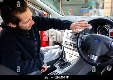 Woodbridge, Suffolk, UK Febbraio 24 2021: Un giovane uomo adulto che pulisce la sua auto. Pulizia dei rifiuti e rimozione dello sporco Foto Stock