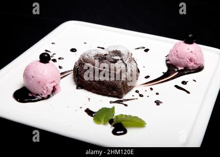 Fondan Dessert cioccolato con gelato su una piastra bianca su sfondo nero. Uno squisito cioccolato francese fondan dessert. Foto Stock