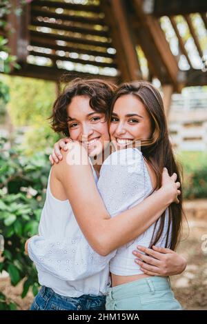 Due giovani ragazze adolescenti abbracciati e sorridenti circondati da piante. Foto Stock