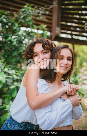 Due giovani ragazze adolescenti abbracciati e sorridenti circondati da piante. Foto Stock