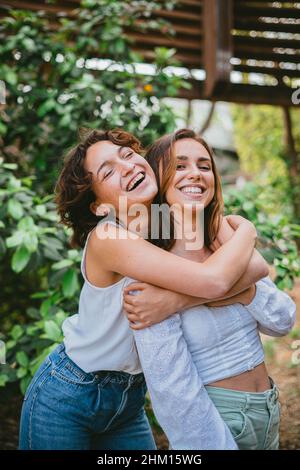 Due giovani ragazze adolescenti abbracciati e ridenti circondati da piante. Stanno divertendosi e sembrano molto felici. Foto Stock