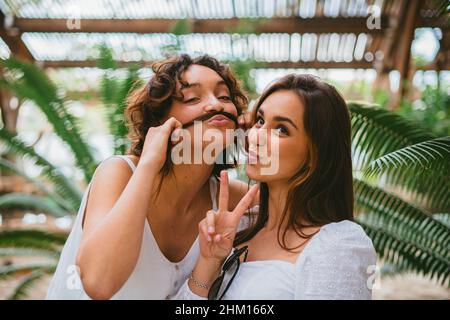 Due ragazze teenager divertenti che guardano la macchina fotografica e sorridono. Uno di loro sta giocando e facendo baffi dei capelli dell'altra ragazza. Foto Stock