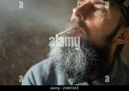 L'uomo con la barba lunga fuma una sigaretta, un ritratto Foto Stock