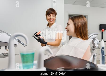 Il dentista sorridente dimostra per il mock-up del paziente delle ganasce umane e spiega la prevenzione e il trattamento delle carie. Modello denti in mani medico. Foto di concetto sul tema dentale. Foto Stock