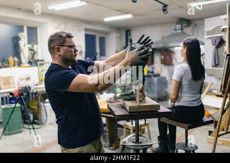 Uomo scultore crea scultura donna uomo in argilla sculpta. Laboratorio di creazione di statue artigianali. Piccola impresa. Foto Stock