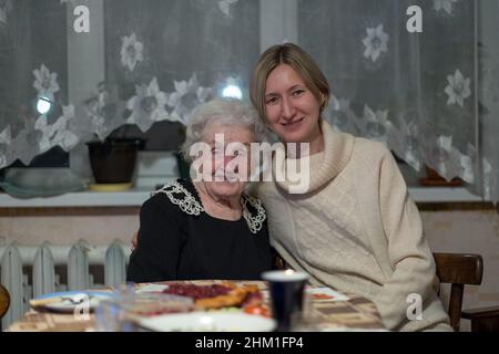 Una donna anziana e sua figlia posano per un ritratto seduto ad un tavolo. Foto Stock