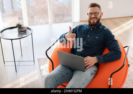 Uomo Freelancer utilizzando il laptop gesturing Thumbs Up seduta a casa Foto Stock