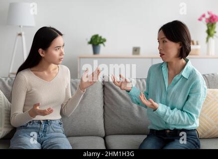Donna asiatica matura infelice e sua figlia adulta che hanno combattuto, litigando l'uno con l'altro sul divano in soggiorno Foto Stock