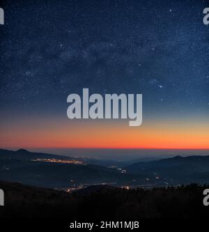 paesaggio di cielo stellato notte con le luci della città e i colori del crepuscolo all'orizzonte Foto Stock