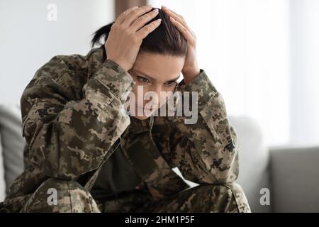 PTSD e veterani. Donna depressa in uniforme militare che tocca la testa nella disperazione Foto Stock