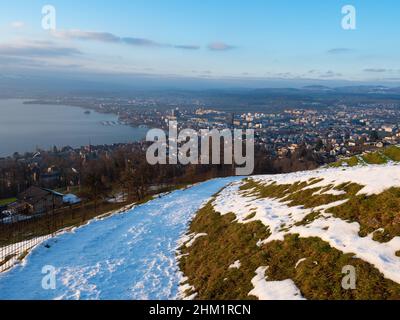 Una pista coperta di neve che conduce alla città di Zug, in Svizzera, in un soleggiato pomeriggio invernale Foto Stock