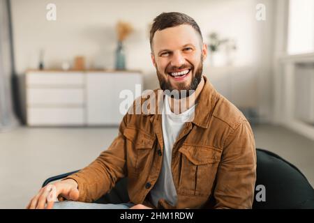 Felice Guy Bearded sorridendo seduto in sedia a casa Foto Stock