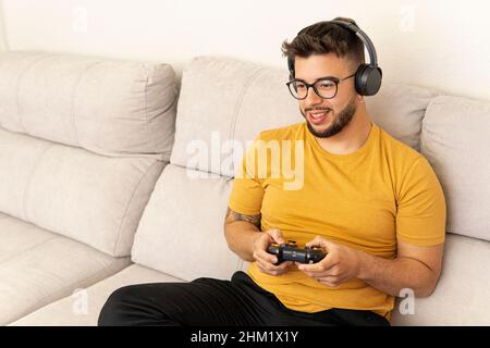 Giovane ragazzo latino con un controller in mano giocando a videogiochi online con i suoi amici e con le cuffie. Foto Stock