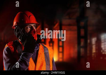 Uomo in respiratore che parla di walkie-talkie durante il fuoco in edificio industriale. Foto Stock