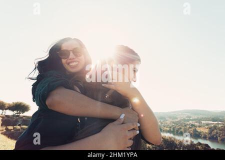 Un paio di donne che si divertono durante una giornata di sole ci si agganata mentre si sorride con la fotocamera con copia spazio Foto Stock