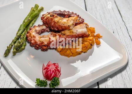 Tentacoli di polpo arrosto con carote e asparagi in piatto bianco su tavole di legno bianco Foto Stock