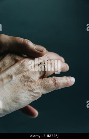 Un paio di vecchie mani che mostrano un anello di gioielli sul dito su uno sfondo scuro Foto Stock