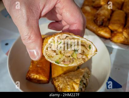 Il cuoco che tiene un mezzo taglio fatto in casa croccante rotolo primavera mostrando la carne e verdura ripieno all'interno. Foto Stock