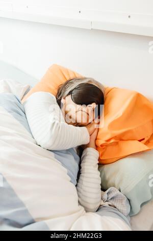 Una vecchia signora che dorme usando una maschera facciale in una camera da letto moderna Foto Stock