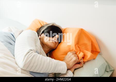 Una vecchia signora che dorme usando una maschera facciale in una camera da letto moderna con spazio di copia Foto Stock