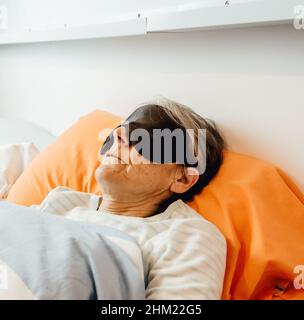 Una vecchia signora che dorme usando una maschera facciale in una camera da letto moderna Foto Stock