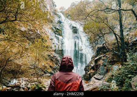 Una donna fuori fuoco in una pelle d'olio viola in piedi di fronte a una cascata gigante Foto Stock