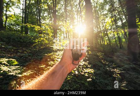 L'uomo del viaggiatore tiene una bussola nella foresta con la luce solare esplosiva. Scatto del punto di vista Foto Stock