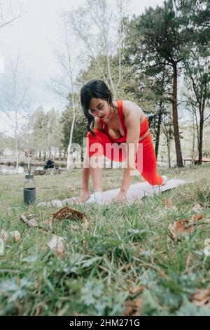 Giovane donna in abbigliamento fitness che fa esercizi di yoga su un tappetino yoga al parco durante una giornata di sole Foto Stock