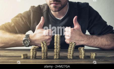 L'uomo mostra pollice in su con le monete impilano sul tavolo di legno, finanza di affari di concetto o investimento Foto Stock