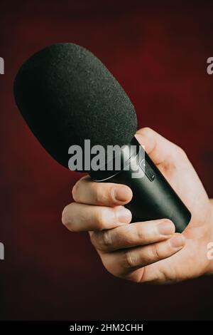 Una mano che afferra un microfono su uno sfondo rosso Foto Stock