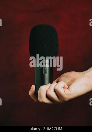 Una mano che afferra un microfono su uno sfondo rosso Foto Stock