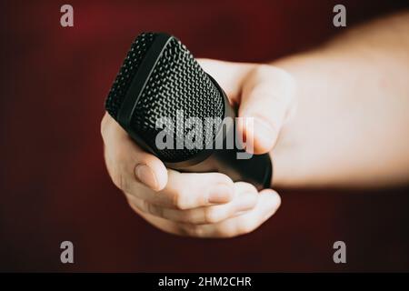 Una mano che afferra un microfono su uno sfondo rosso Foto Stock