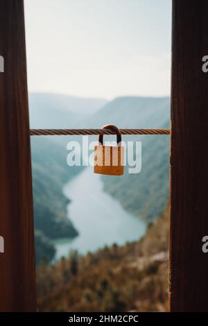 Lucchetto singolo appeso a un cordone di fronte a un fiume massiccio con concetto di amore e fedeltà Foto Stock