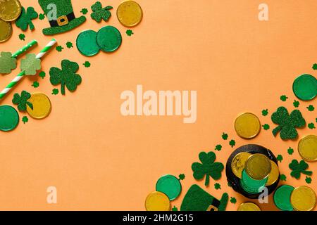 Banner giorno San Patrizio con monete d'oro, foglie di shamrock di trifoglio, pentola d'oro, cappelli di leprechauns su sfondo arancione. Disposizione piatta, vista dall'alto. San Patricks Foto Stock