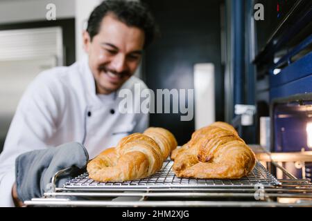 Giovane uomo latino panettiere e forno croissant e pane in cucina in Messico America Latina Foto Stock