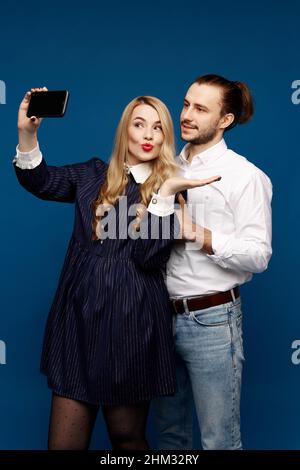 Una bella donna bionda che prende un selfie con un bel giovane uomo sullo sfondo blu Foto Stock